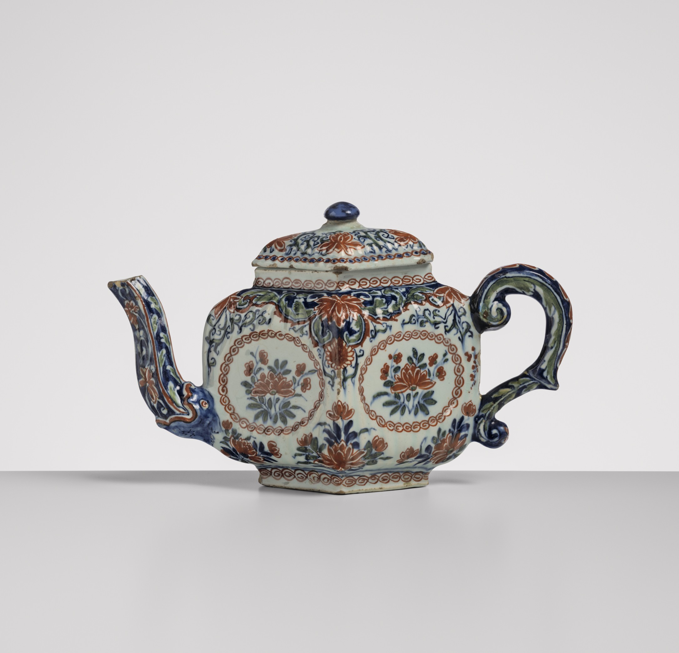 Theepot met kleurrijke bloem- en bladmotieven, een gebogen tuit, sierlijk oor en bijpassend deksel.