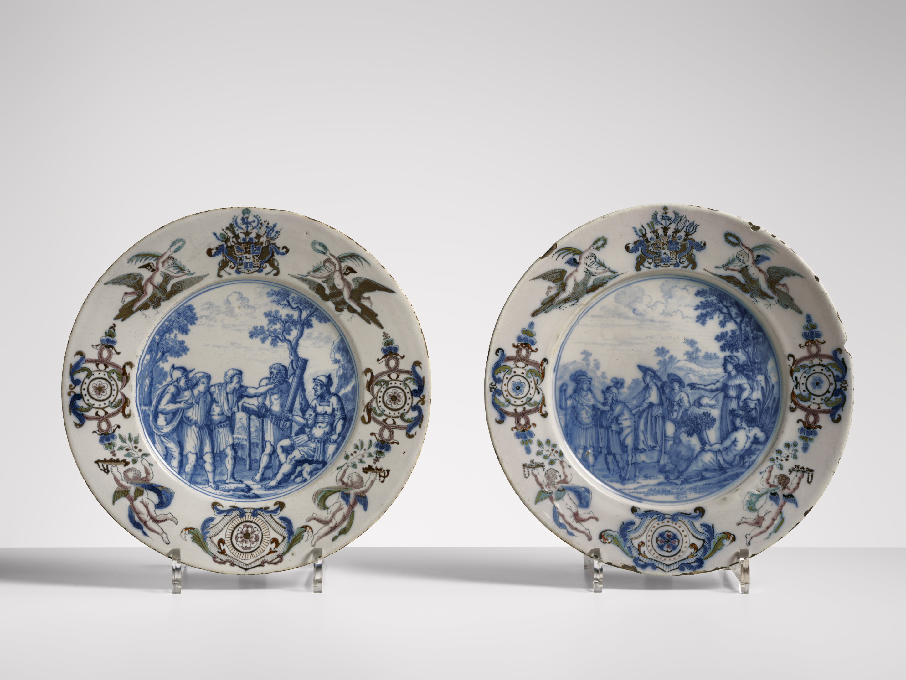 Twee Delfts blauwe decoratieve borden met blauw-witte schilderingen van landschappen en figuren, naast elkaar afgebeeld.